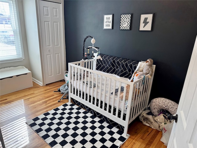 bedroom featuring a closet, a crib, baseboards, and wood finished floors