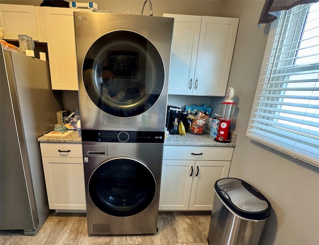 laundry room featuring stacked washing maching and dryer, light wood-style flooring, and cabinet space