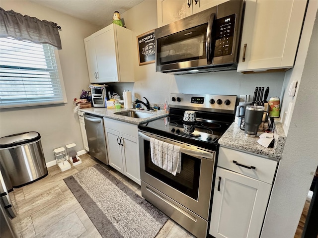 kitchen featuring light stone counters, stainless steel appliances, white cabinetry, a sink, and baseboards