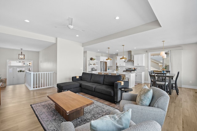 living area with ceiling fan with notable chandelier, light wood-type flooring, baseboards, and recessed lighting