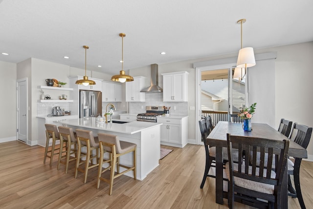 kitchen with open shelves, stainless steel appliances, light countertops, a sink, and wall chimney range hood