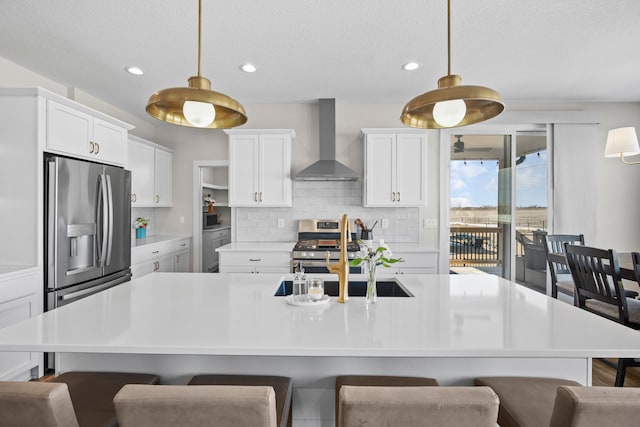 kitchen with a sink, light countertops, wall chimney range hood, appliances with stainless steel finishes, and decorative backsplash