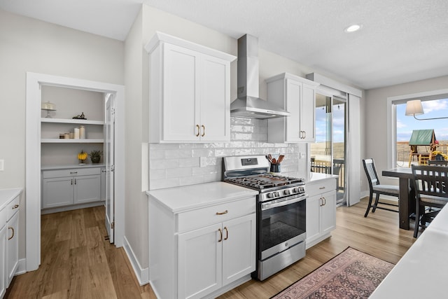 kitchen featuring light countertops, wall chimney range hood, light wood-type flooring, and stainless steel range with gas stovetop