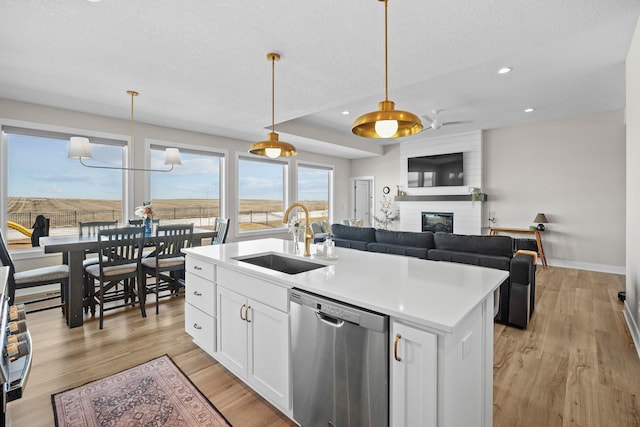 kitchen featuring a large fireplace, a sink, white cabinets, light wood-style floors, and stainless steel dishwasher