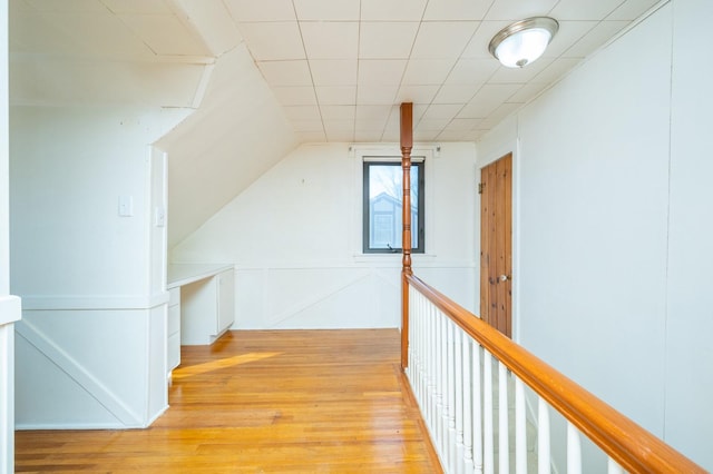 hall with lofted ceiling, light wood-style floors, and an upstairs landing