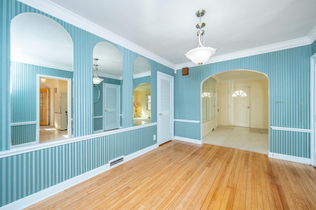 unfurnished room featuring arched walkways, ornamental molding, wood-type flooring, and wallpapered walls