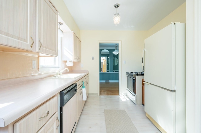 kitchen featuring dishwashing machine, a sink, light countertops, stainless steel range with gas cooktop, and freestanding refrigerator