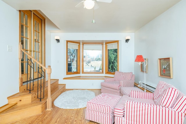 living area featuring a baseboard radiator, stairway, a ceiling fan, wood finished floors, and baseboards