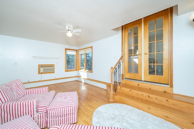 living area featuring baseboards, ceiling fan, wood finished floors, a wall mounted air conditioner, and stairs