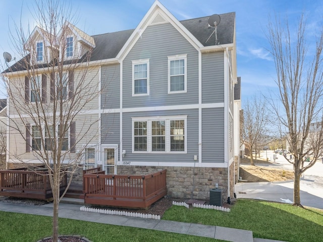 view of front facade featuring a shingled roof, central AC, a deck, stone siding, and a front lawn