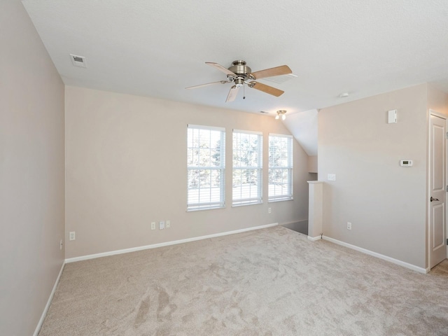 carpeted empty room featuring lofted ceiling, baseboards, visible vents, and a ceiling fan