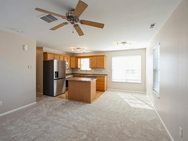 kitchen with light carpet, visible vents, a kitchen island, stainless steel appliances, and a sink