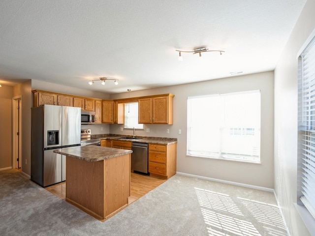 kitchen featuring light colored carpet, appliances with stainless steel finishes, a sink, a kitchen island, and baseboards