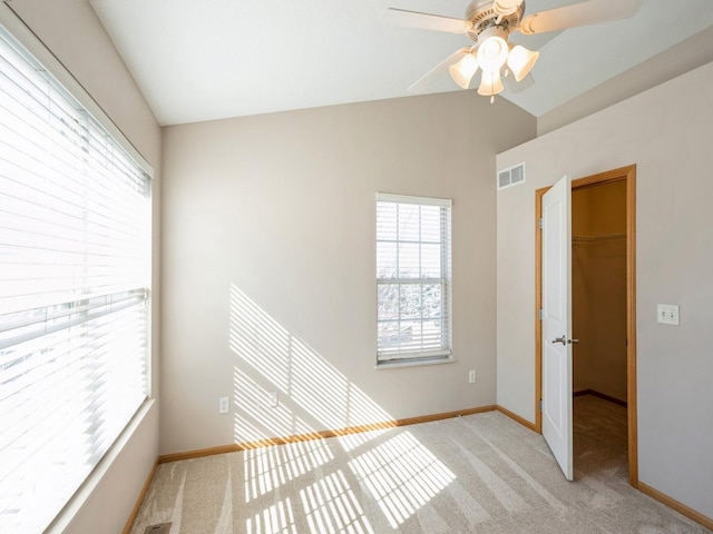 empty room with visible vents, a ceiling fan, light carpet, vaulted ceiling, and baseboards