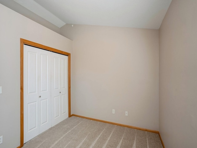 unfurnished bedroom with a closet, light colored carpet, vaulted ceiling, and baseboards