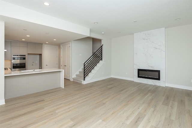 unfurnished living room featuring stairway, light wood-style floors, a fireplace, a sink, and recessed lighting