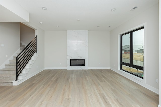 unfurnished living room with stairs, a premium fireplace, light wood-style flooring, and baseboards