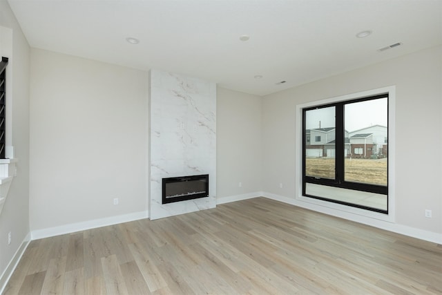 unfurnished living room featuring baseboards, visible vents, a high end fireplace, light wood-style floors, and recessed lighting