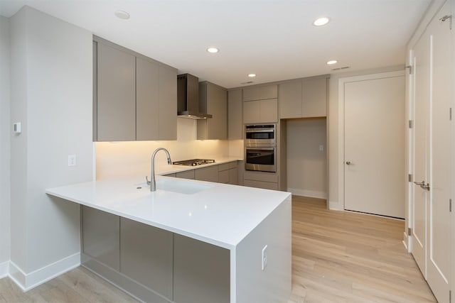 kitchen featuring modern cabinets, appliances with stainless steel finishes, a peninsula, gray cabinetry, and wall chimney range hood