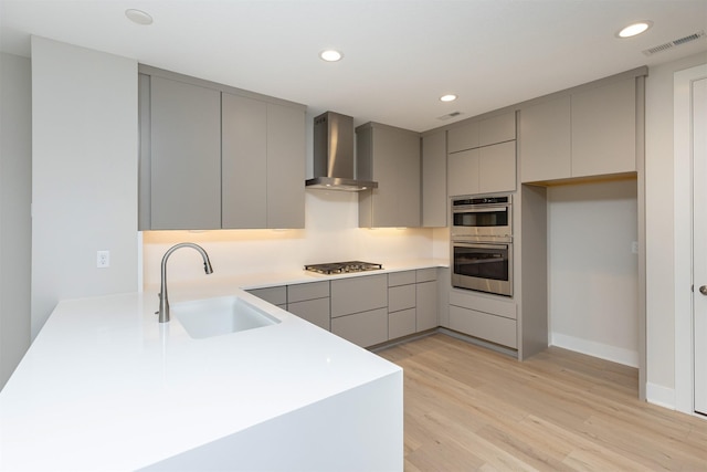 kitchen featuring stainless steel appliances, a sink, wall chimney range hood, gray cabinets, and modern cabinets