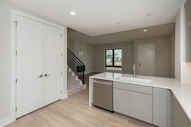 kitchen with light wood-style flooring, a peninsula, a sink, light countertops, and stainless steel dishwasher