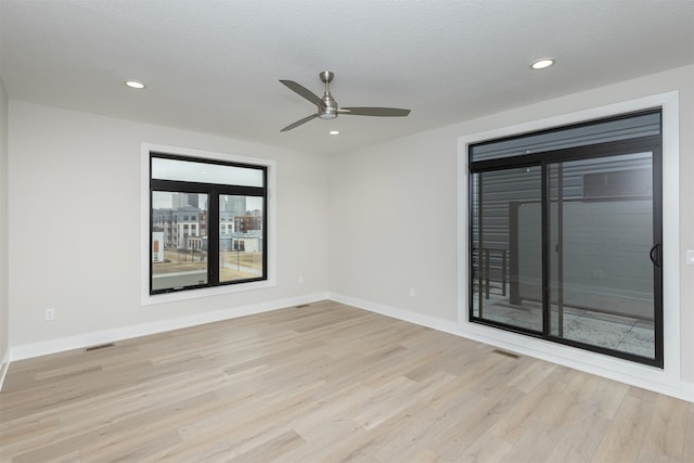 unfurnished room with light wood-style floors, visible vents, a textured ceiling, and baseboards