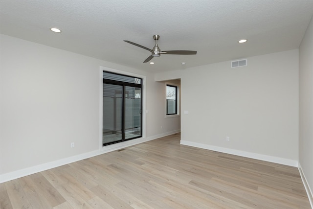 unfurnished room with light wood-type flooring, baseboards, visible vents, and a textured ceiling