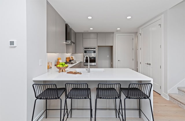 1160 Murphy St, Des Moines, IA 50309 - kitchen featuring gray cabinets, wall chimney range hood, a peninsula, modern cabinets, and light wood finished floors