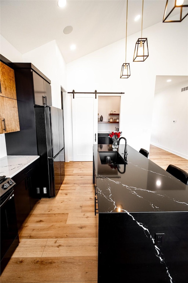 kitchen with decorative light fixtures, light wood finished floors, a barn door, black range with gas cooktop, and a sink