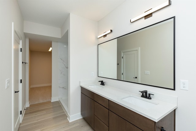 bathroom with double vanity, walk in shower, a sink, and wood finished floors