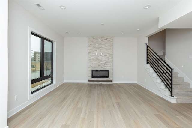 unfurnished living room featuring light wood-style floors, baseboards, a fireplace, and stairway