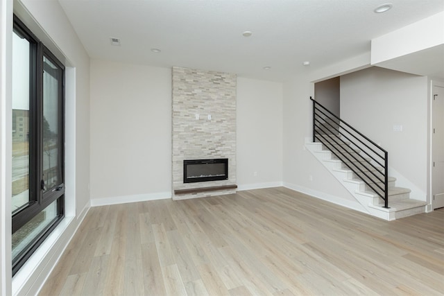 unfurnished living room with light wood-type flooring, visible vents, a fireplace, and stairway