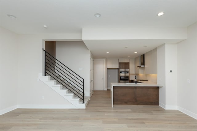 1166 Murphy St, Des Moines, IA 50309 - kitchen with wall chimney exhaust hood, light countertops, light wood-style flooring, baseboards, and a peninsula