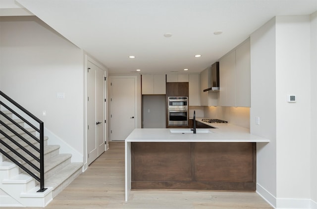 kitchen with a peninsula, light countertops, wall chimney range hood, gas stovetop, and a sink