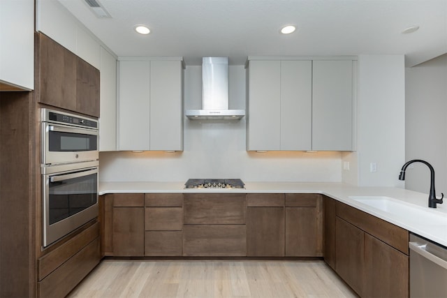 kitchen featuring stainless steel appliances, light countertops, visible vents, a sink, and wall chimney exhaust hood