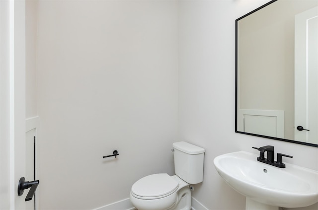 half bath with toilet, baseboards, and a sink