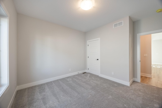 empty room featuring carpet floors, visible vents, and baseboards