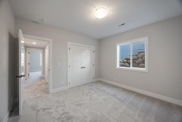 unfurnished bedroom with a closet, light colored carpet, visible vents, a textured ceiling, and baseboards