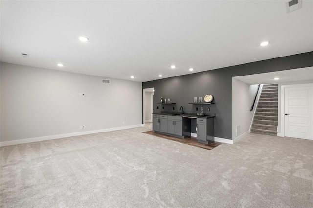 unfurnished living room featuring stairs, light carpet, indoor wet bar, and visible vents