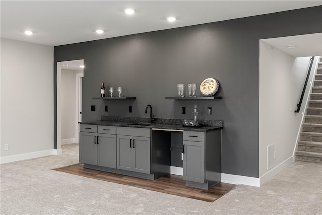 bar featuring light carpet, stairway, indoor wet bar, and a sink