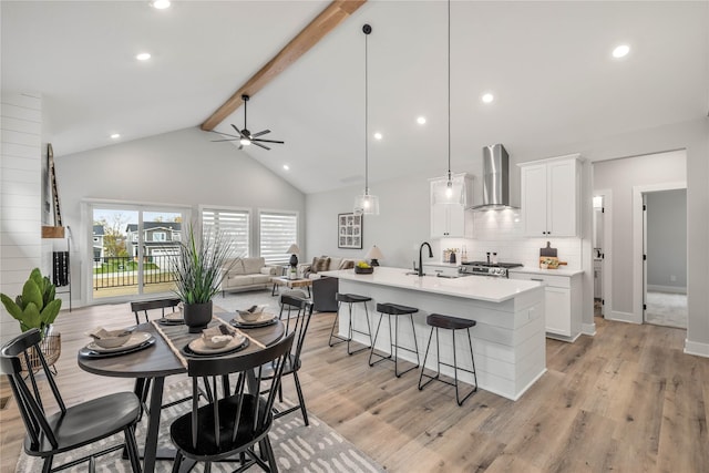 kitchen featuring a breakfast bar area, stove, light wood-style floors, beamed ceiling, and wall chimney exhaust hood