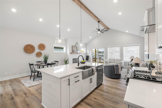 kitchen with open floor plan, beam ceiling, light wood-type flooring, stainless steel dishwasher, and a sink