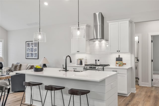 kitchen featuring stainless steel range with gas cooktop, white cabinetry, a sink, wall chimney range hood, and a kitchen breakfast bar