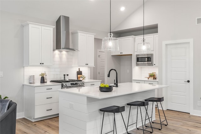 kitchen with lofted ceiling, stainless steel appliances, white cabinetry, light wood-style floors, and wall chimney exhaust hood