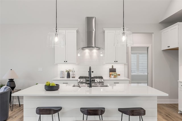 kitchen featuring a kitchen bar, white cabinetry, decorative backsplash, and wall chimney exhaust hood