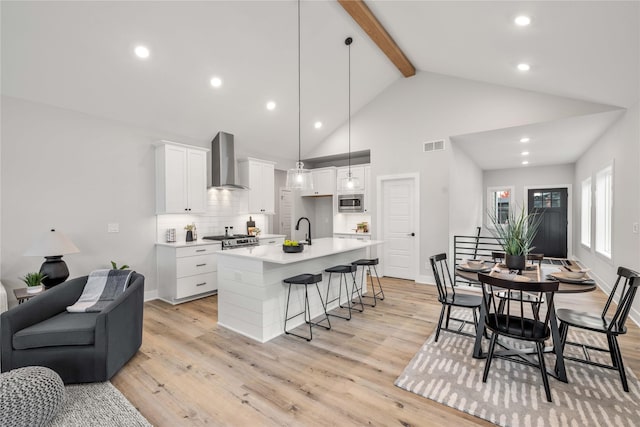 kitchen with light wood finished floors, visible vents, stainless steel microwave, wall chimney range hood, and a kitchen bar