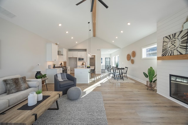 living room featuring baseboards, visible vents, light wood-style floors, a fireplace, and high vaulted ceiling