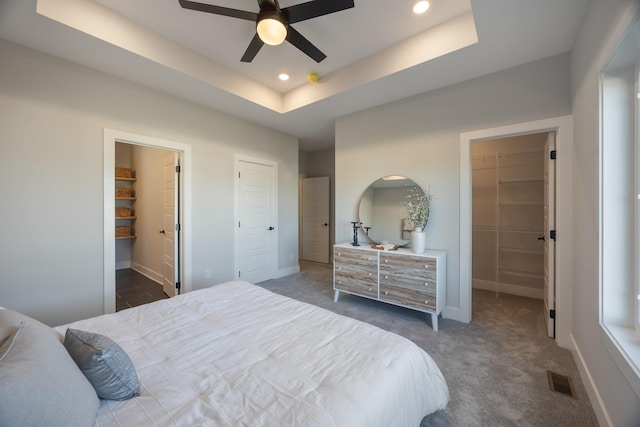 bedroom featuring a spacious closet, dark carpet, a raised ceiling, and visible vents