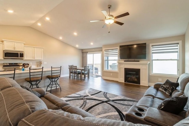 living area featuring vaulted ceiling, a glass covered fireplace, dark wood finished floors, and a ceiling fan