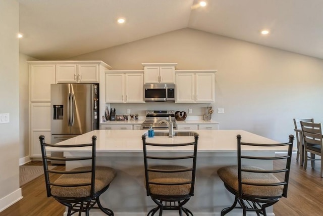 kitchen featuring a center island with sink, white cabinets, dark wood-type flooring, vaulted ceiling, and stainless steel appliances